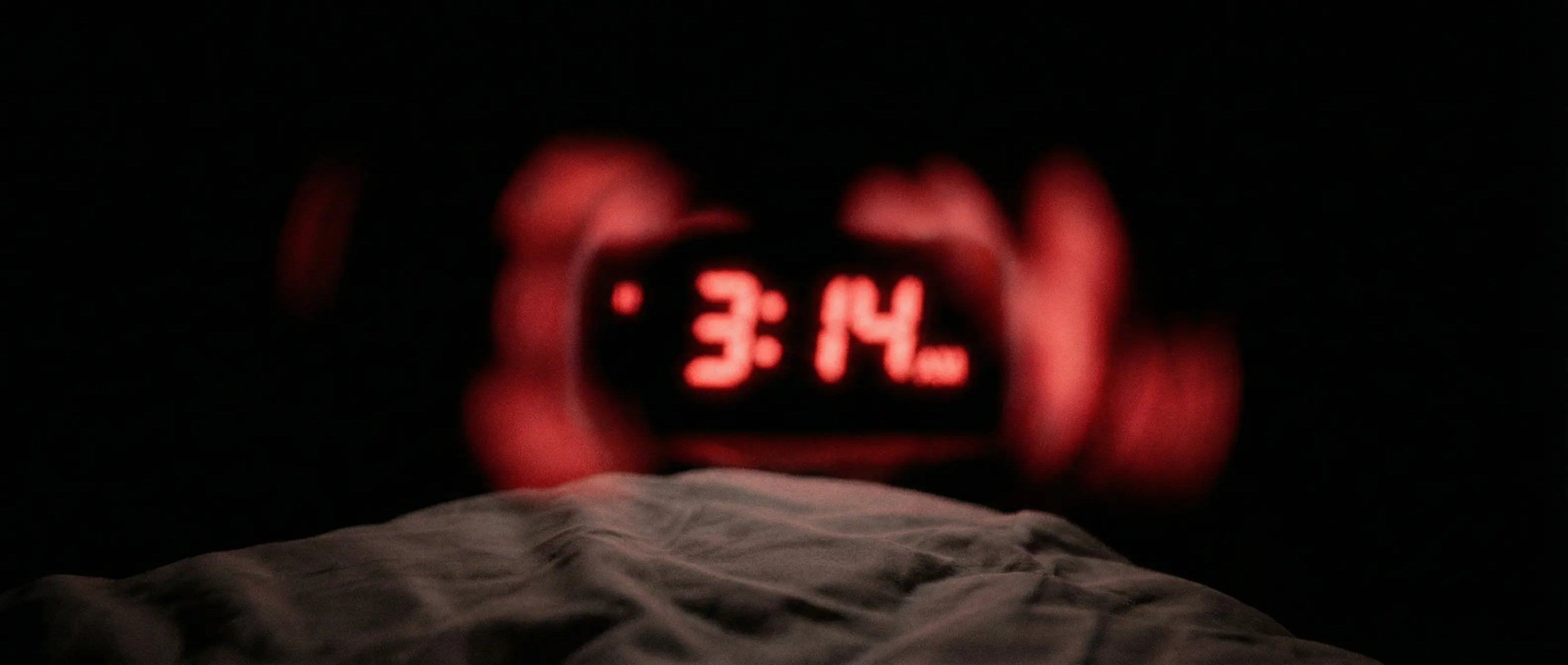 blurry digital clock at 3 AM in the dark, representing sleep anxiety and waking up tired.